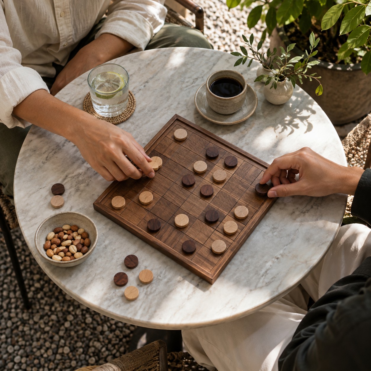Illustrative scene: Two adult friends playing a simple board game at an outdoor café, hands and sleeves only, plain wooden pieces without lettering, overhead view.
